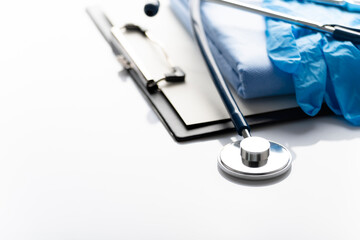 Healthcare medical background with copy-space of stethoscope, clipboard, gloves and folded overalls on white table