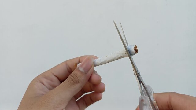 An Asian man's hand cuts a cigarette against a white background, symbolizing quitting smoking, health awareness, and breaking bad habits. Perfect for anti-smoking campaigns or healthy lifestyle conten