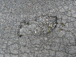 Close-up of a damaged asphalt road surface with cracks and a pothole