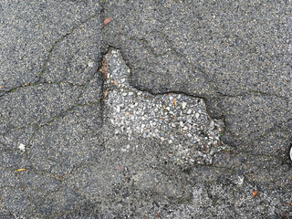 Close-up of damaged asphalt with cracks and a pothole, showing texture and detail