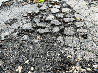 Close-up of damaged asphalt road surface with cracks and potholes