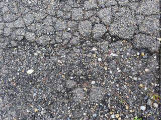 Cracked asphalt texture with small rocks and pebbles, a detailed close-up