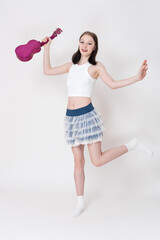 Positive playful young woman ukulelist and cheerleader holding ukulele in her hand and dancing on...