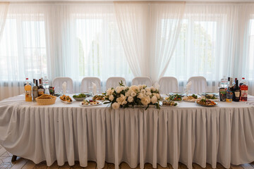 Elegant White Wedding Table Setup with Floral Arrangement and Buffet Food Display in Bright Sunlit Room