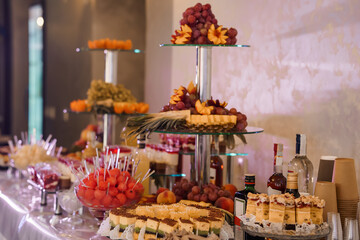 Elegant multi-tiered fruit and dessert display at luxury event with grapes, berries, cakes, and beverages arranged on glass stands