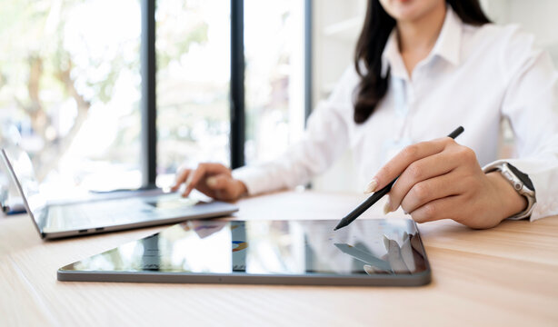 Close-up of a businesswoman using a digital tablet and stylus pen while working on a laptop. - Powered by Adobe