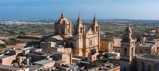 Aerial view of Mdina, Malta shows St. Pauls Cathedral with twin towers, clock faces, and dome,...