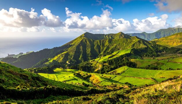 Lush, rolling hills and verdant valleys meet the bright, blue ocean under a partly cloudy sky, illuminated by sunlight. The landscape is vibrant