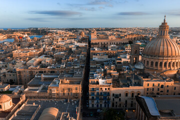Obraz premium Aerial sunset view of Valletta, Malta shows limestone blocks, Baroque forms, the basilica dome on the right, a straight street to Grand Harbour, and long evening shadows.