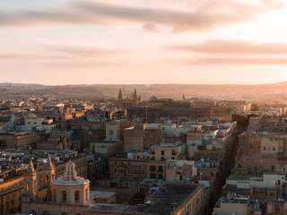 Obraz premium Aerial view of Valletta, Malta at golden hour, warm light on limestone blocks, church domes and twin spires, narrow streets lead to the harbor, long shadows add depth.