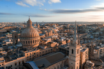 Fototapeta premium Aerial panorama of Valletta, Malta at sunset shows Our Lady of Mount Carmel dome and St. Pauls Anglican Pro Cathedral spire above limestone blocks and narrow streets.