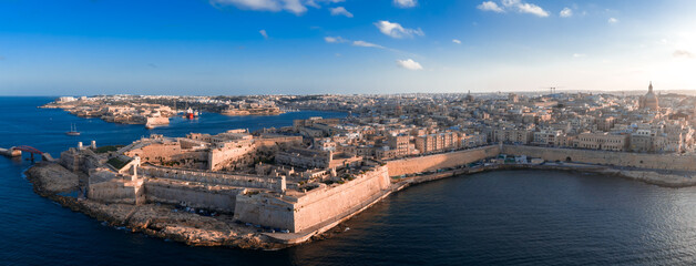 Aerial view of Valletta, Malta at sunset shows bastion walls, domes, and spires. The Grand Harbour...