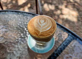 The perspective of a cup of hot latte art coffee on the table and blurred background.