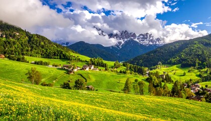 Obraz premium Lush green meadows leading to a village nestled in a valley. Towering peaks are partially covered by clouds under a blue sky