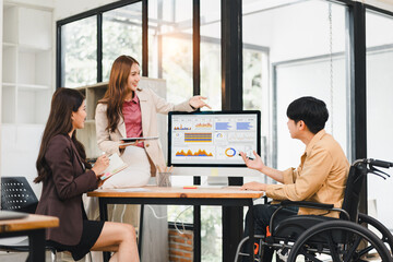 Diverse business team with colleague in wheelchair analyzing data dashboard in inclusive workplace meeting