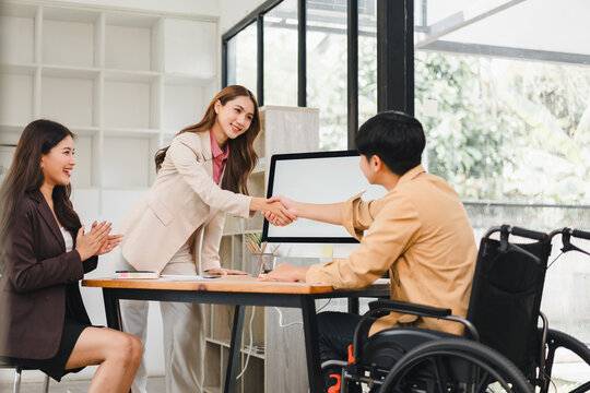 Businesswoman shaking hands with man in wheelchair, Diverse team celebrating success or agreement in inclusive workplace