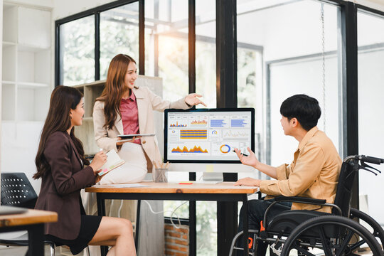 Diverse business team with colleague in wheelchair analyzing data dashboard in inclusive workplace meeting