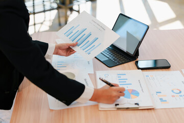 Business analyst reviewing sales chart and financial report with tablet and smartphone on wooden desk, focused and productive
