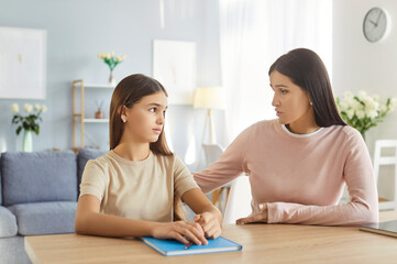 Loving and caring mother assisting teenage daughter with homework and engaging in a supportive...
