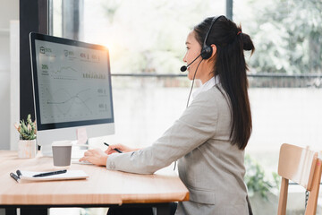 Young woman wearing headset at computer desk viewing analytics chart, focused and professional