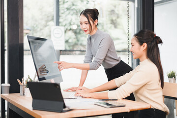 Young woman pointing at desktop monitor while colleague types on keyboard in modern office, collaborative teamwork and focused discussion