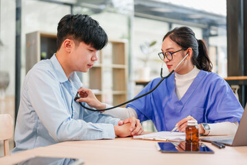 Fototapeta premium Young patient and nurse in clinic using stethoscope during checkup, calm supportive scene