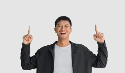 A young Asian man wearing a black coat happy smiling pointing thumbs up isolated on a grey background. A man who looks happy to get first place