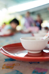 Empty white plastic bowl placed on red dish on wooden table, close up with soft focus and space for text.