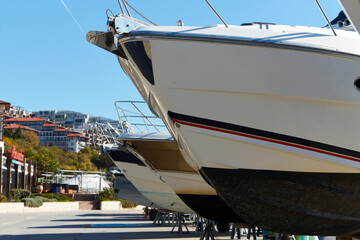 On a sunny day, yachts lined up in their winter storage berths at the marina, showcasing their elegant hulls and vibrant colours against a backdrop of clear blue skies and distant buildings