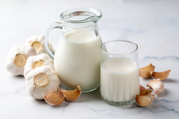 Hot garlic milk in a glass cup with peeled garlic on the background