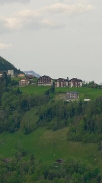 Scenic landscape of green hills with charming village and distant mountains in Switzerland captured during springtime
