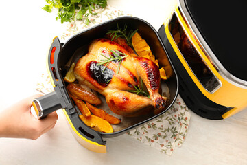 Woman cooking chicken and vegetables in air fryer at white wooden table, top view