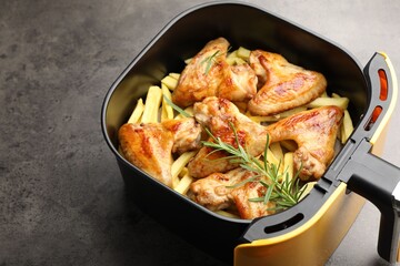 Grilled chicken wings and french fries with rosemary in air fryer basket on grey table, closeup. Space for text