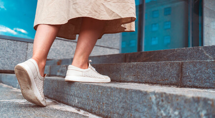 Young girl is walking up the stairs in the city, female legs in white shoes closeup.