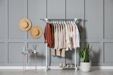 Women's clothes hanging on rack, hats, houseplant and coffee table with decor near grey wall indoors