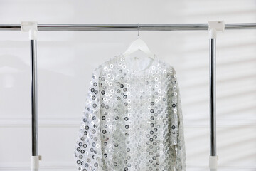 Stylish dress hanging on rack near white wall