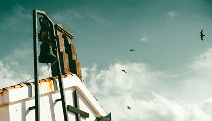 A small chapel with a bell tower, a Christian church against a bright sky background with flying birds.