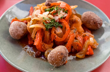 Delicious dish with a cod fillet fish, boiled potatoes and peppers on the red background.
