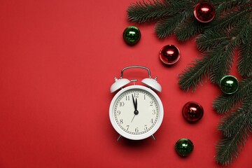 Alarm clock, fir tree branches and baubles on red background, flat lay with space for text. New Year greeting card