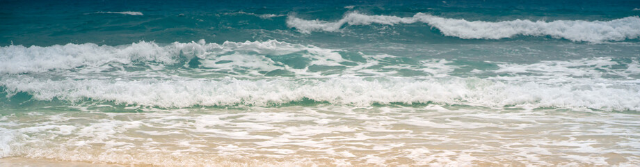 A sandy beach on the coastline of the ocean with clear water with small waves.