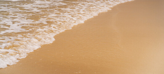 Clean sandy beach by the ocean, small waves with foam washing the shore, close-up view of golden yellow sand from copy space. © Zhanna