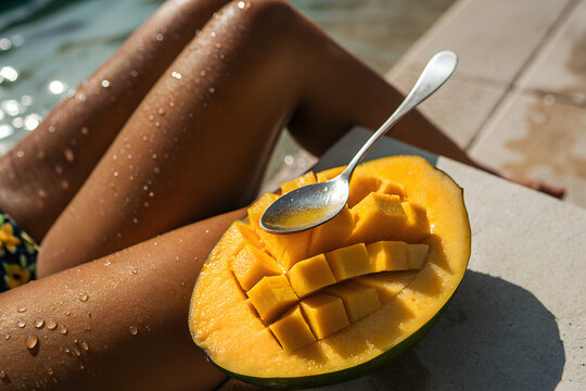 Woman enjoying a fresh, juicy mango while sunbathing by the pool. Concept of a tropical summer vacation, healthy lifestyle, and pure relaxation.
 Generative Ai.