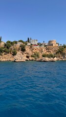 The historic white buildings and an ancient round stone tower of Antalya's Kaleici Old Town stand precariously atop the rocky cliffs, overlooking the intense blue of the Mediterranean Sea