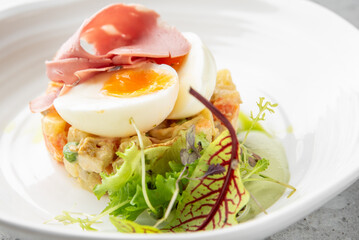 A close-up shot of a gourmet salad with poached eggs, ham, and fresh greens, served on a white plate.
