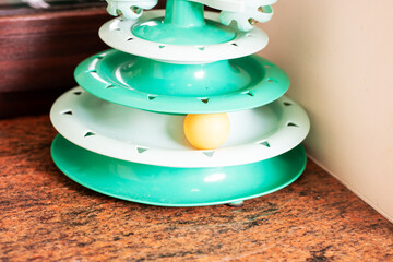 Green plastic cat toy stacked tiers ball trapped in lowest track on scratched wooden table corner