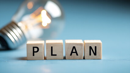 "PLAN" is spelled out in wooden blocks with a bright lightbulb. planning is key to new ideas and success.