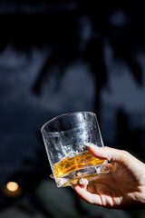 A close-up of a hand holding a glass with amber drink in dramatic lighting, emphasizing contrast, texture, and elegance of minimal beverage concept.