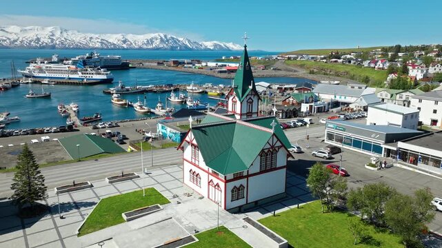 Aerial footage of Husavik harbour and church in one frame. Fishing boats and local architecture highlight the charm of North Iceland.