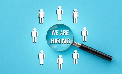 A magnifying glass is used to look at a group of people. The people are drawn as silhouettes and are labeled We are Hiring. Concept of opportunity and growth