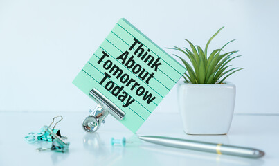 A green plant sits on a table with a piece of paper that says Think about tomorrow